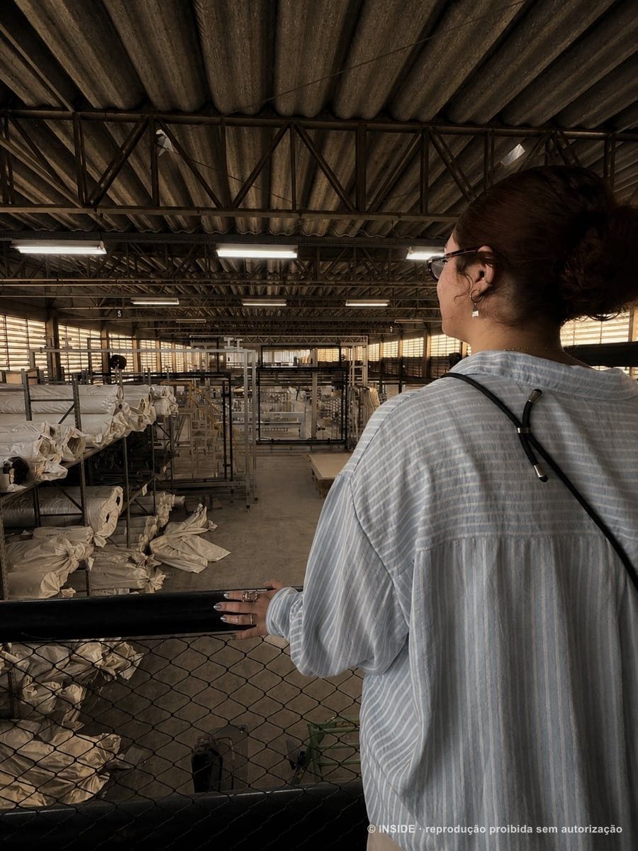 Nicolli Pacheco no galpão da fábrica de tapetes Santa Mônica, entre as peças em produção, bastidores INSIDE, 2026, acervo INSIDE