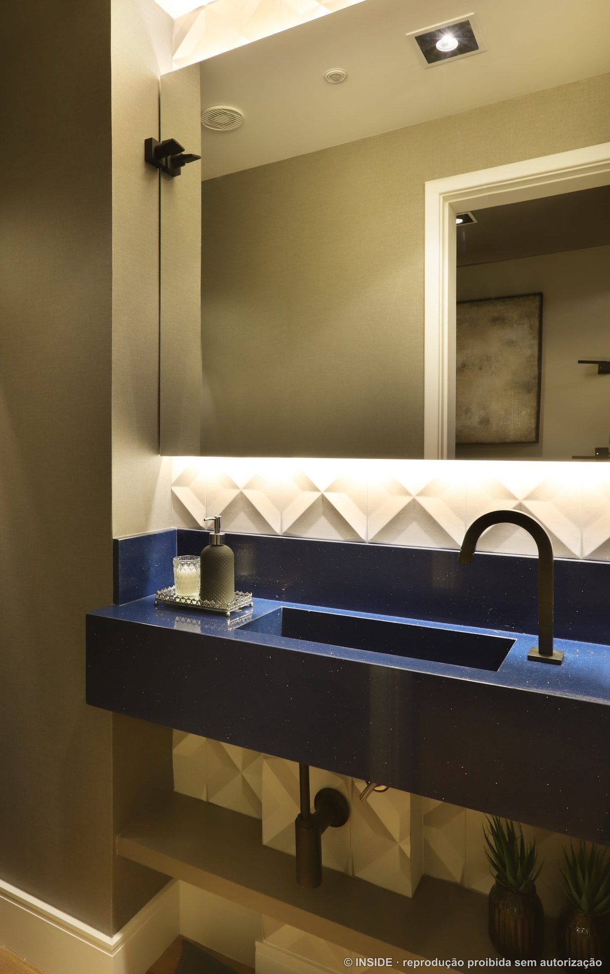 Lavabo com cuba escura esculpida, metais dourados, espelho iluminado e revestimento geométrico em tons de bege, projeto INSIDE
