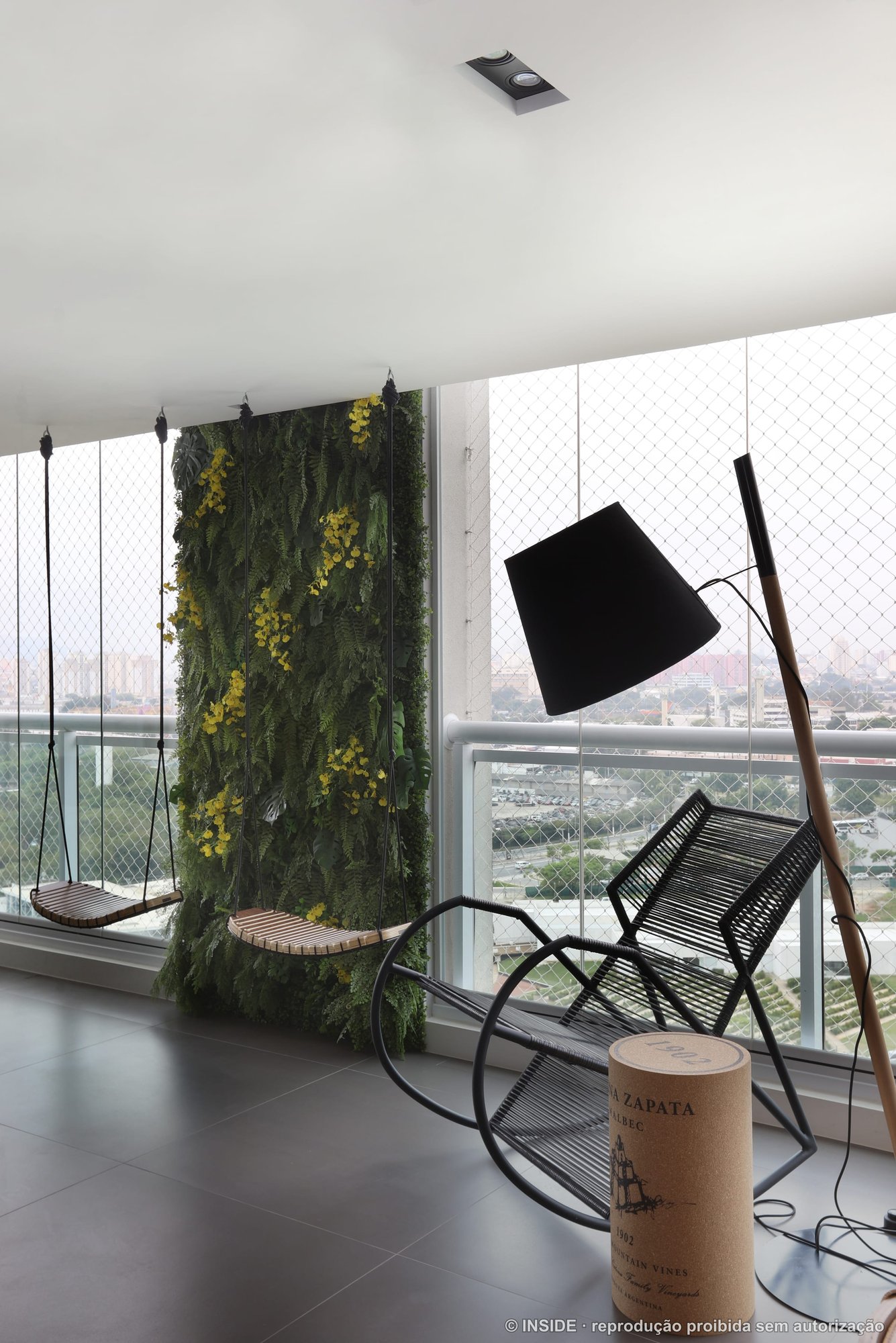 Terraço com jardim vertical florido, poltronas e luminária de piso, com a cidade ao fundo, projeto INSIDE