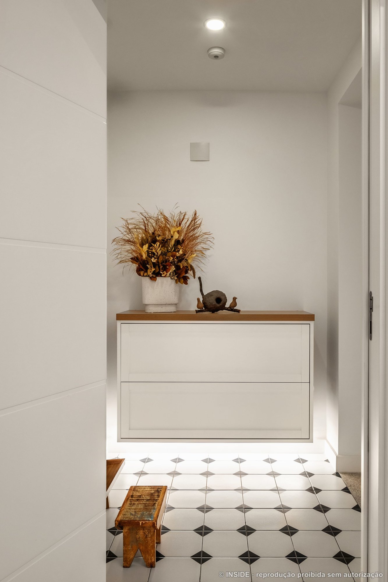 Hall de entrada com aparador suspenso em madeira, vaso de flores secas e piso octogonal preto e branco, projeto INSIDE